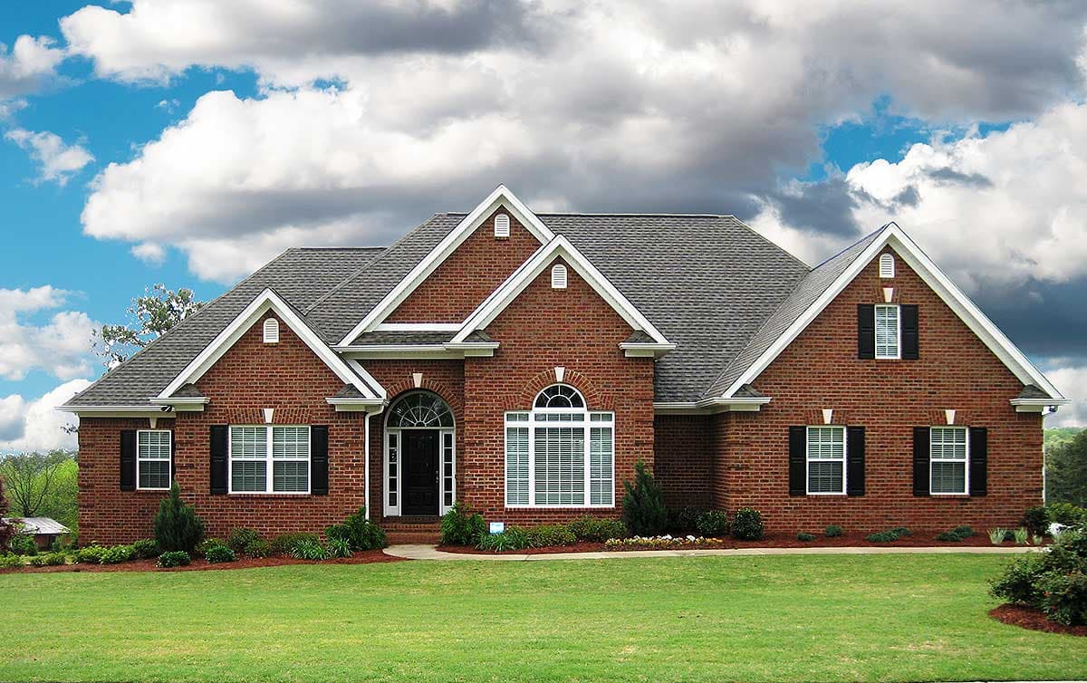 House plan exterior: Red brick two-story home with multiple gables, arched entryway, dormer window, and dark shutters.