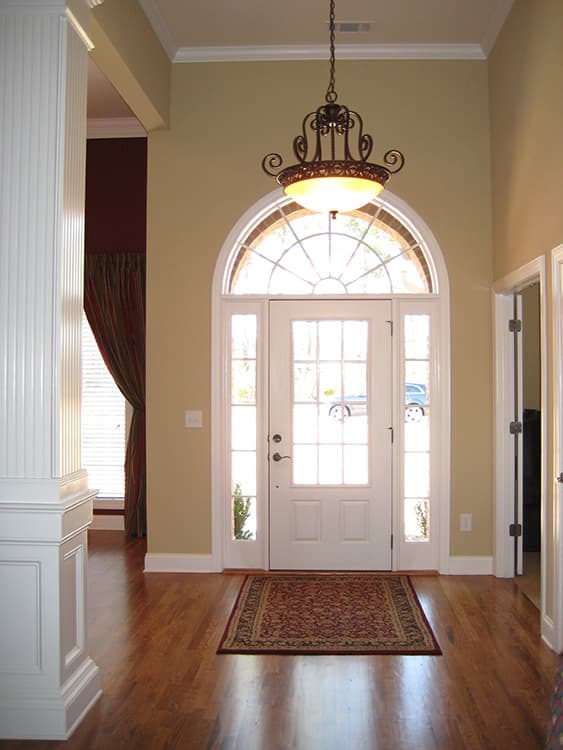 Foyer with double entry doors, transom window, paneled columns, hardwood floors, and chandelier.
