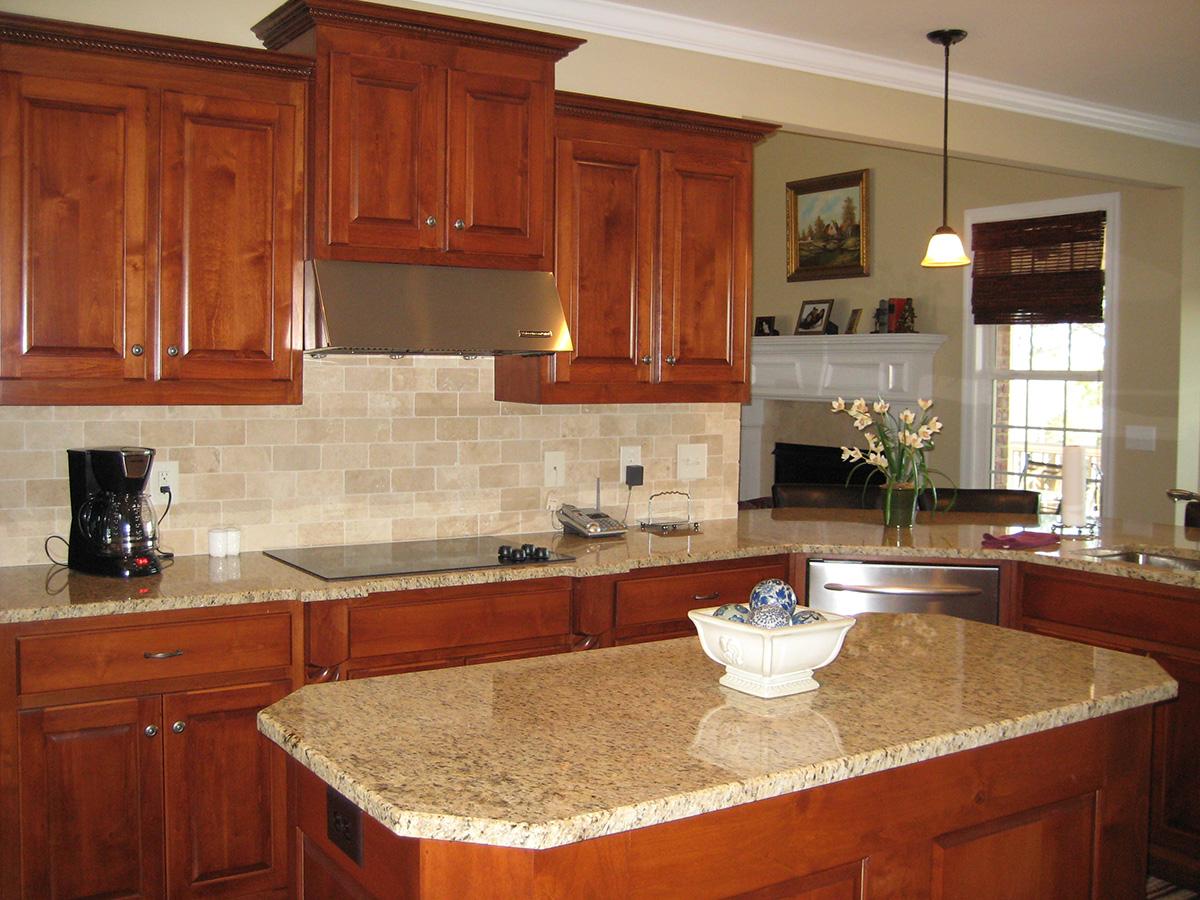 Kitchen with cherry cabinets, granite countertops, stainless steel appliances, and a travertine tile backsplash. Fireplace visible in background.