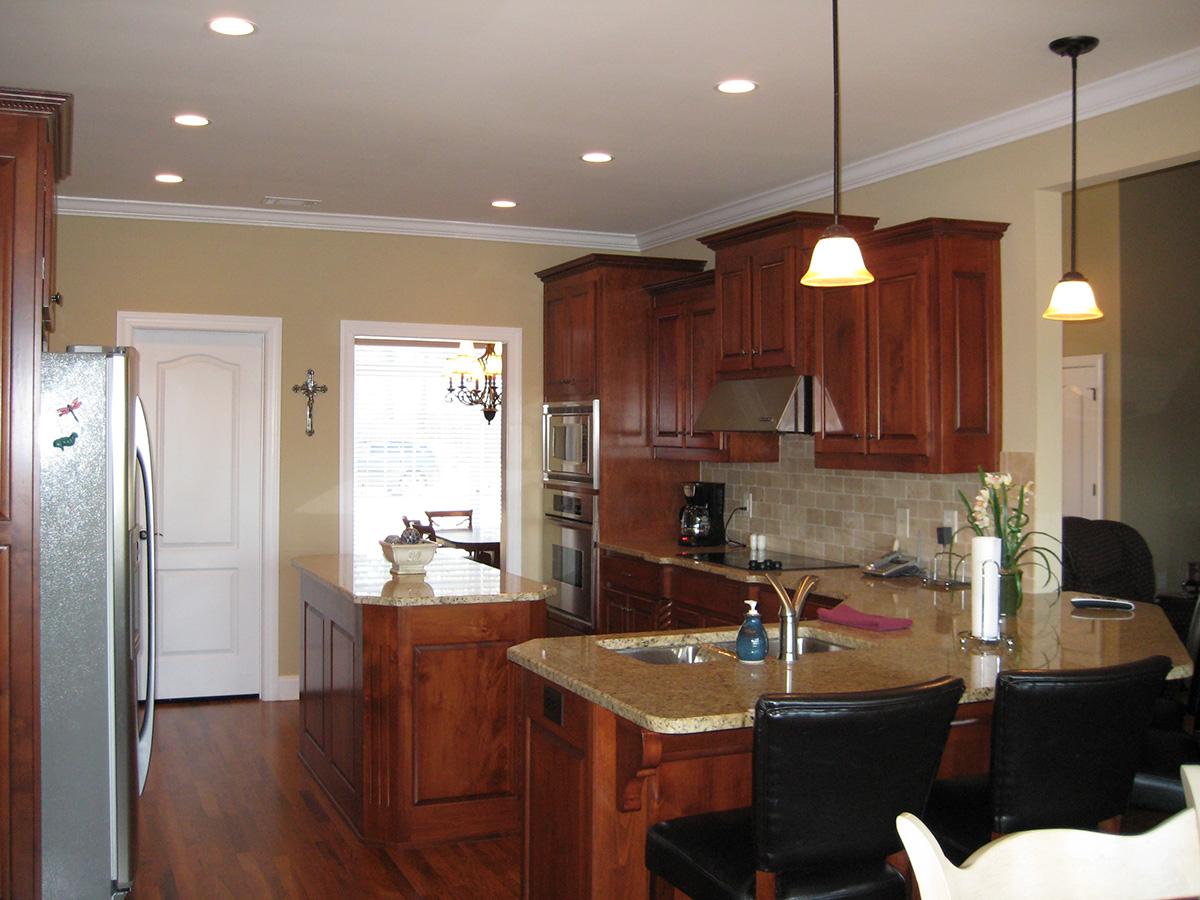 Kitchen with wood cabinetry, granite countertops, large island with sink, stainless steel appliances, and pendant lighting.