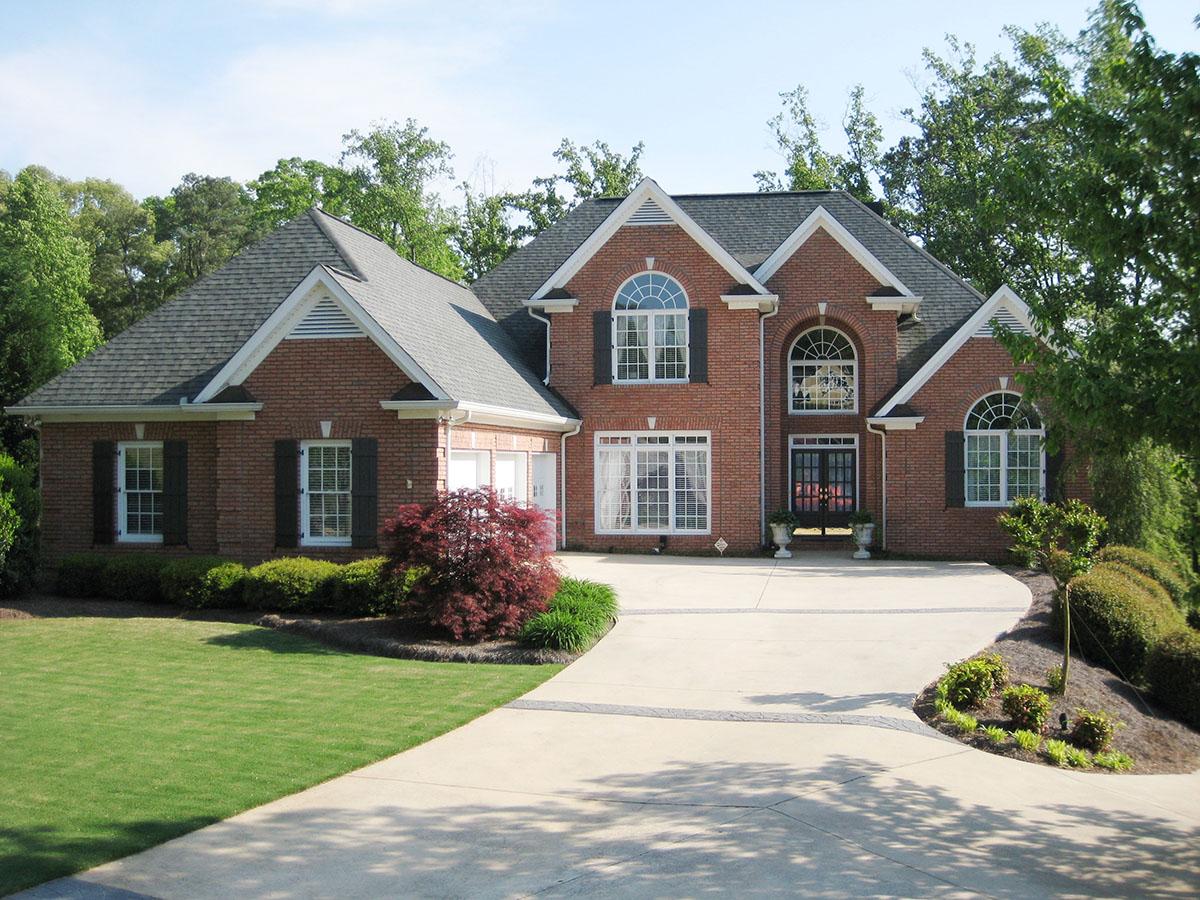 House plan exterior: Red brick two-story home with prominent gables, arched windows, and a central double-door entry.