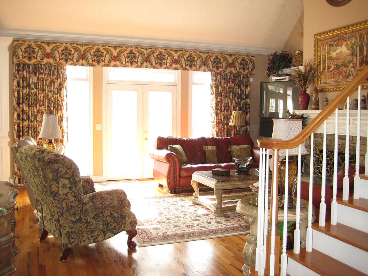 Living room with red leather sofa, patterned armchair, ornate coffee table, fireplace, and staircase.