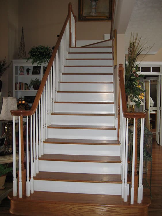 Interior view of a white staircase with wooden treads and railings, leading to an upper level.