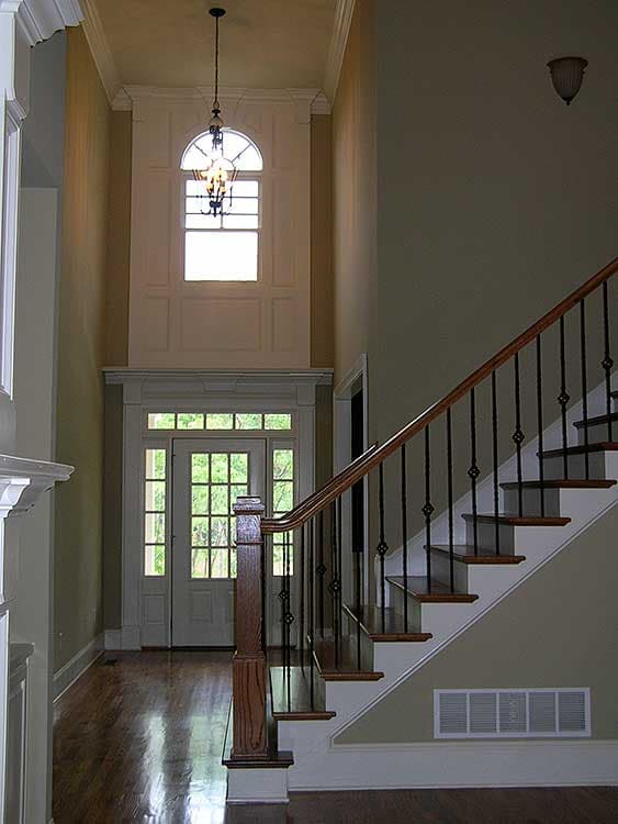Interior view of a foyer with a grand staircase, paneled wall, and arched transom window above double doors.