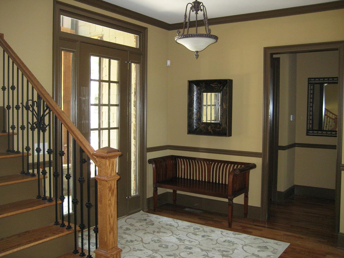 Entryway with wooden stairs featuring black metal balusters, glass-paned door, and decorative bench.