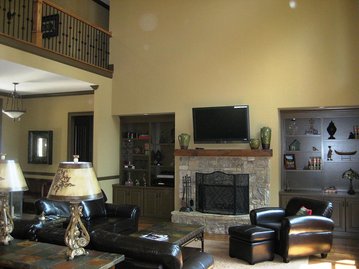 Interior view of a living room with a stone fireplace, TV, built-in shelves, and a balcony overlooking the space.