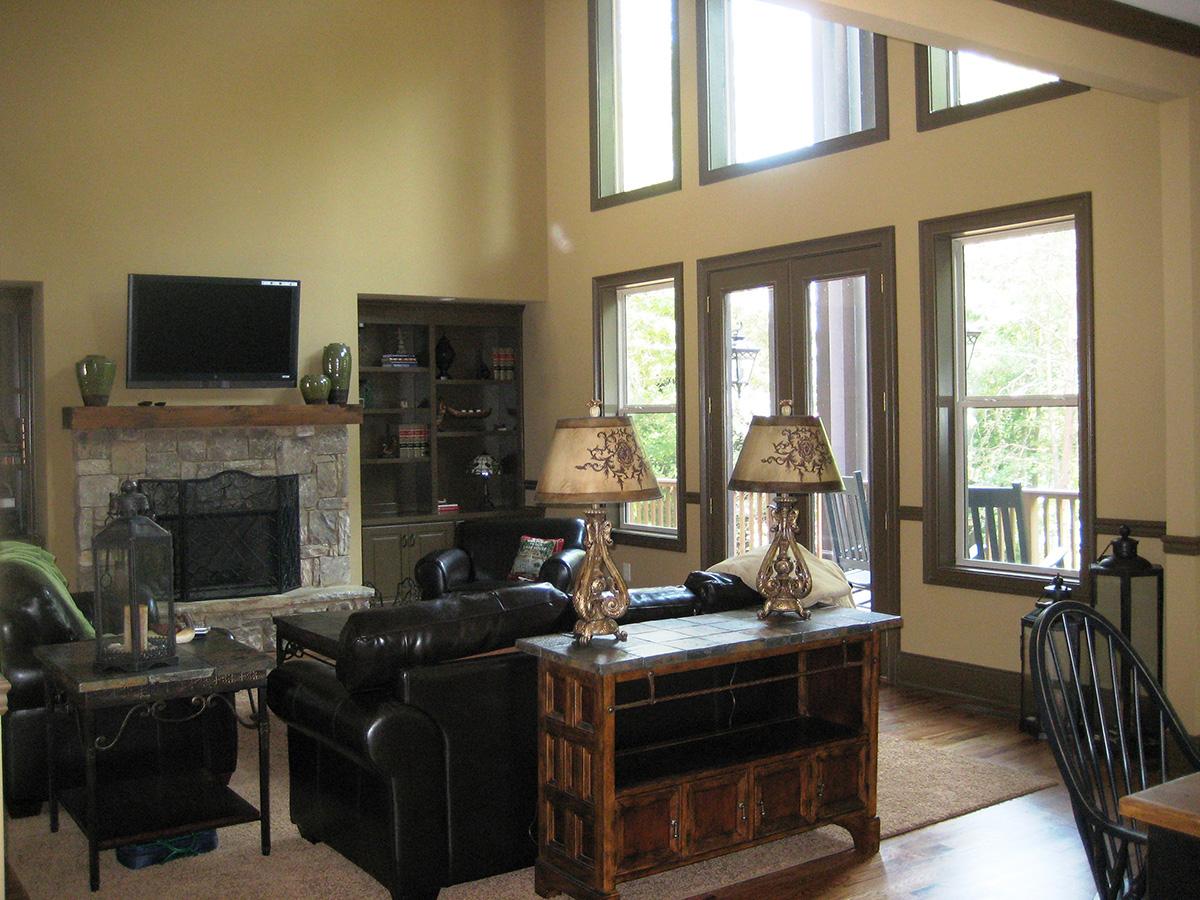 Great room with vaulted ceiling, stone fireplace, built-in shelves, and large windows. Double doors lead to an outdoor deck.