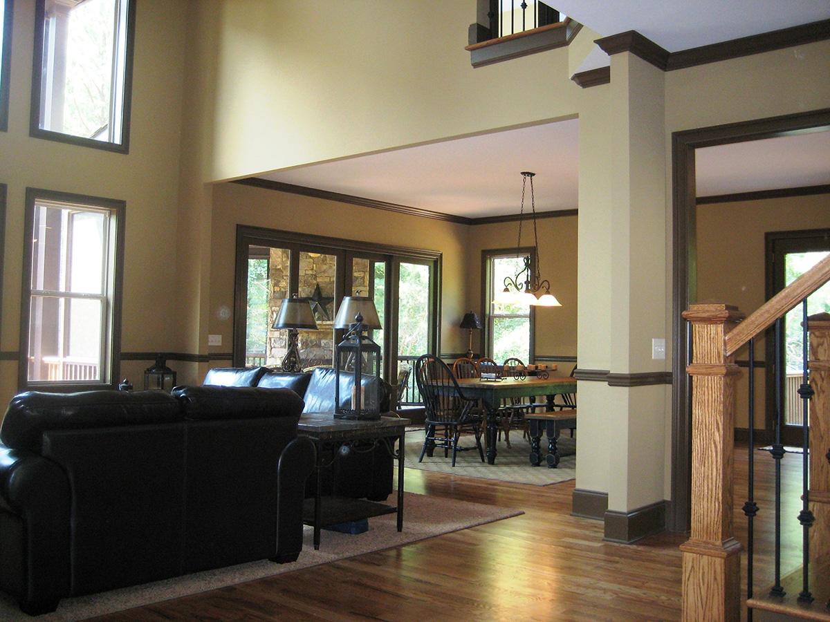 Open-concept living and dining area with a large fireplace and windows, featuring dark leather sofas and wooden dining set.
