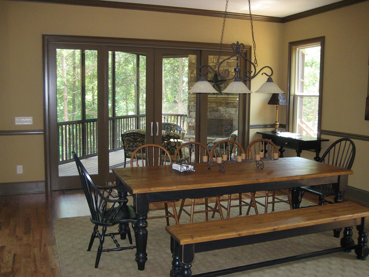 Dining area with wooden table, bench, and chairs, featuring sliding glass doors leading to a screened porch with a stone fireplace visible.