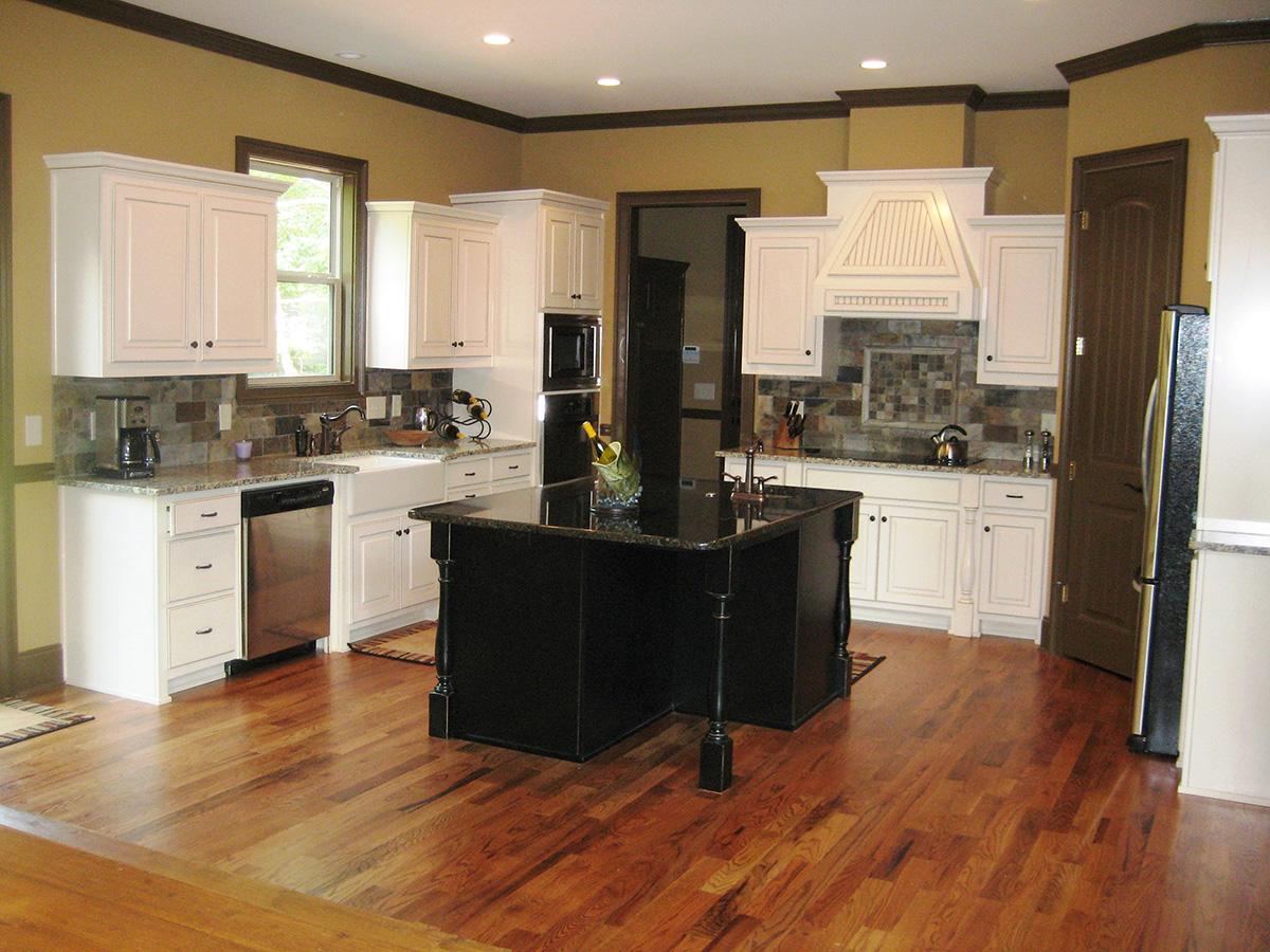 Kitchen with white cabinets, large black island, farmhouse sink, granite countertops, and stainless steel appliances.