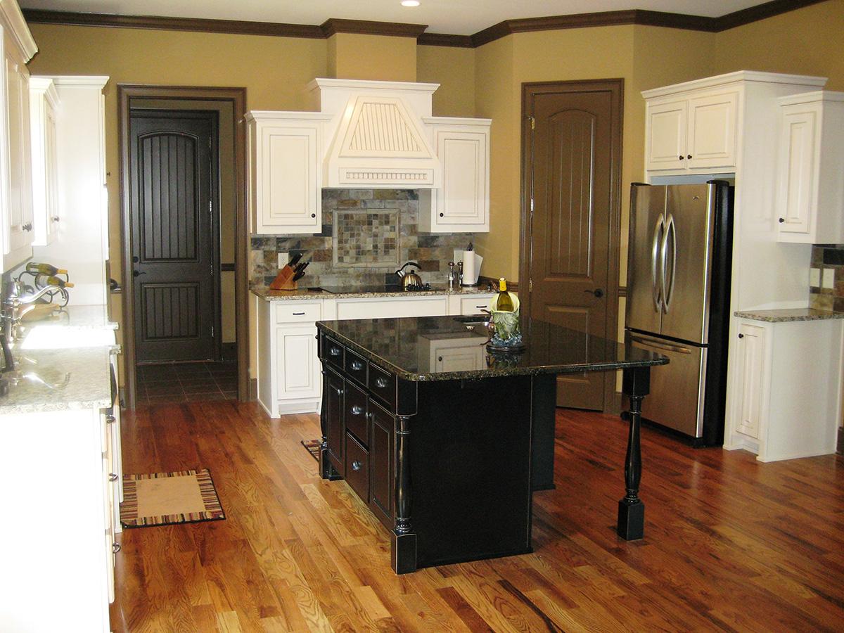 Kitchen with white cabinets, dark island with granite countertop, stainless steel refrigerator, and hardwood floors.