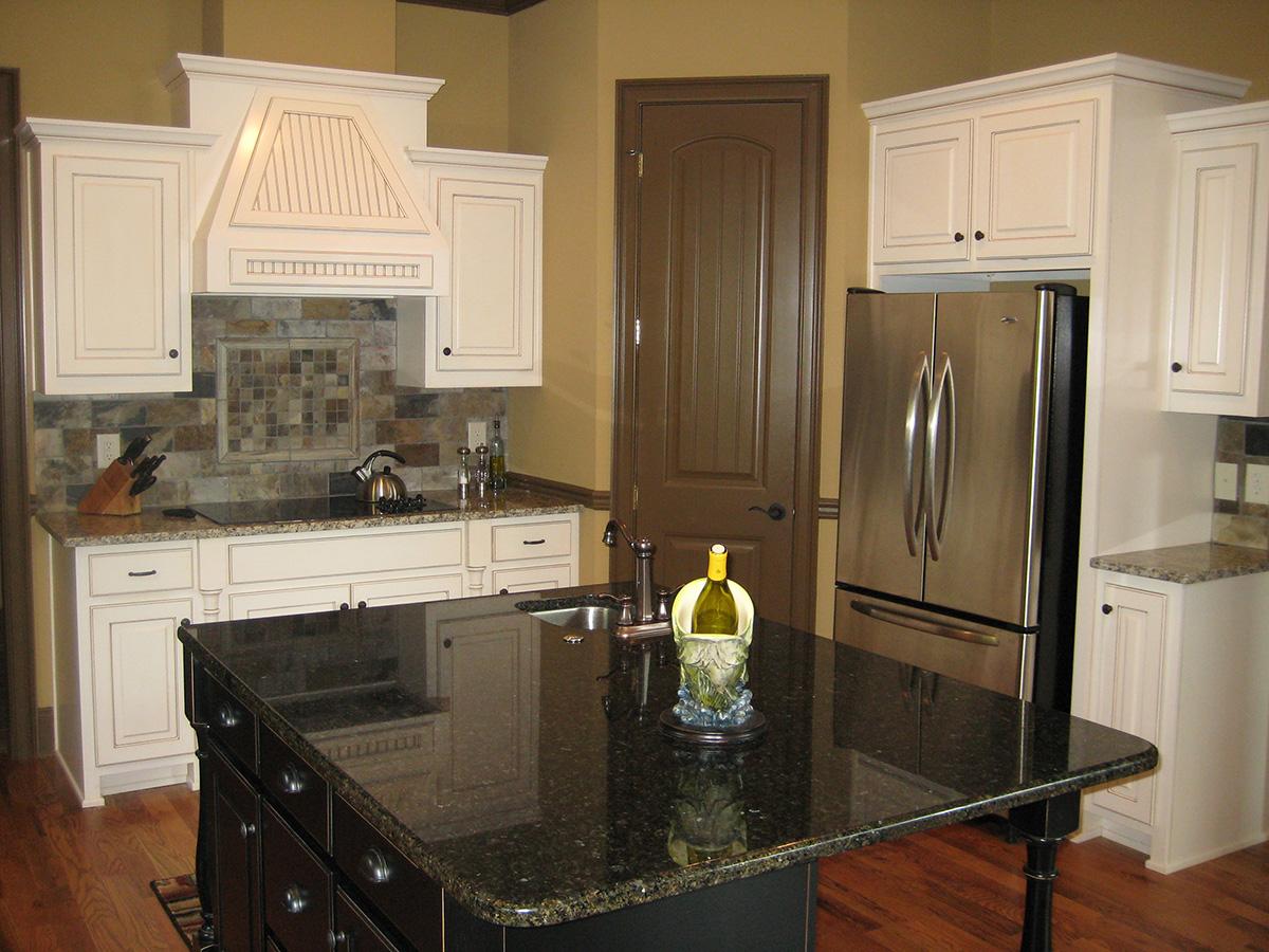 Kitchen with island, stainless steel refrigerator, dark granite countertops, and decorative range hood.