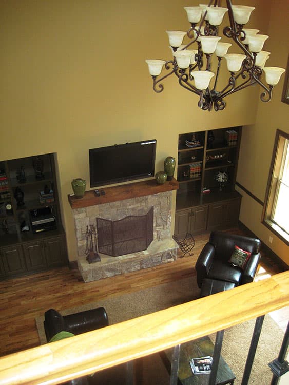 Great room with stone fireplace, built-in shelving, leather furniture, and multi-tiered chandelier viewed from above.