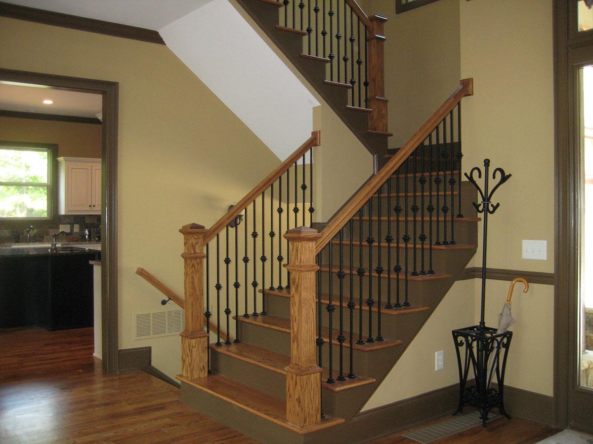 Interior view of a staircase with oak banisters, black balusters, and a view into a kitchen.