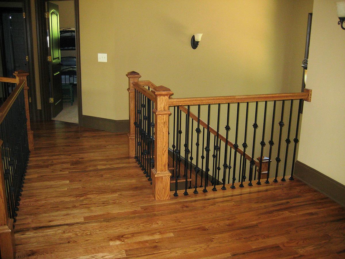 Interior hallway with wooden floors, oak banister, and wrought iron stair railing. Open doorway reveals another room.