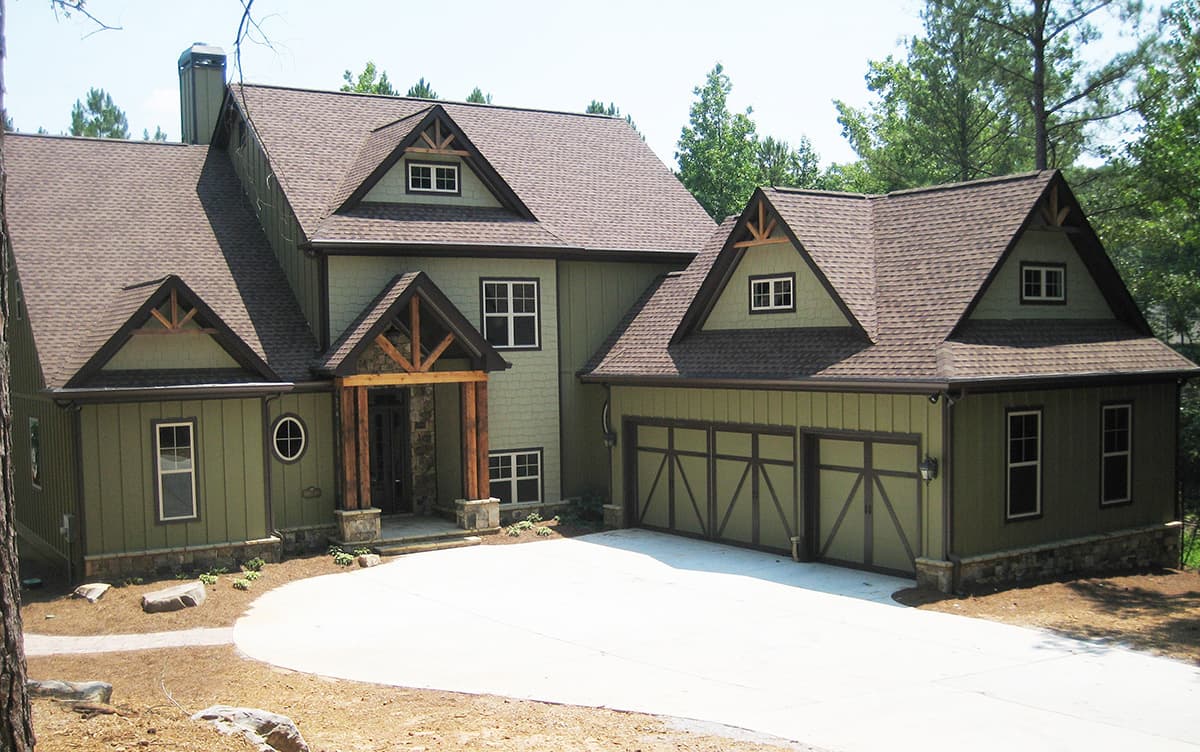 House plan exterior with gabled dormers, exposed rafter tails, prominent front porch with stone base, and a three-car garage.