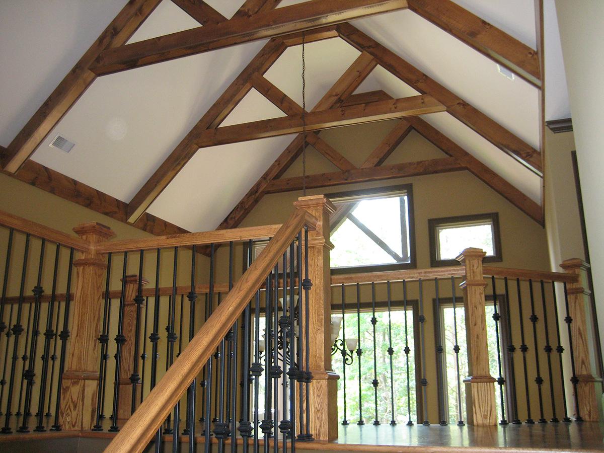 Interior view of a loft with exposed wooden beams, vaulted ceiling, and a wooden railing with black balusters.