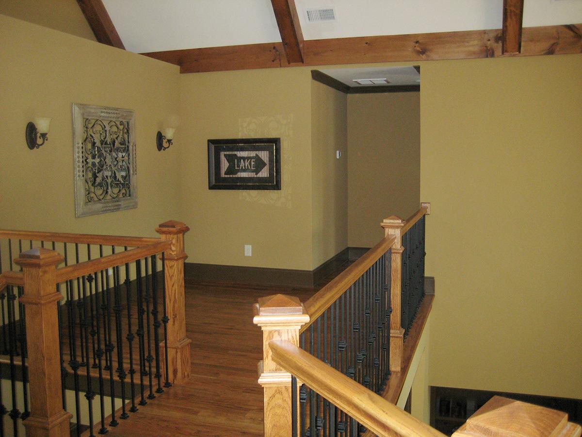 Interior view of a hallway with exposed wood beams on ceiling, a wooden staircase with wrought iron balusters, and decorative wall art.