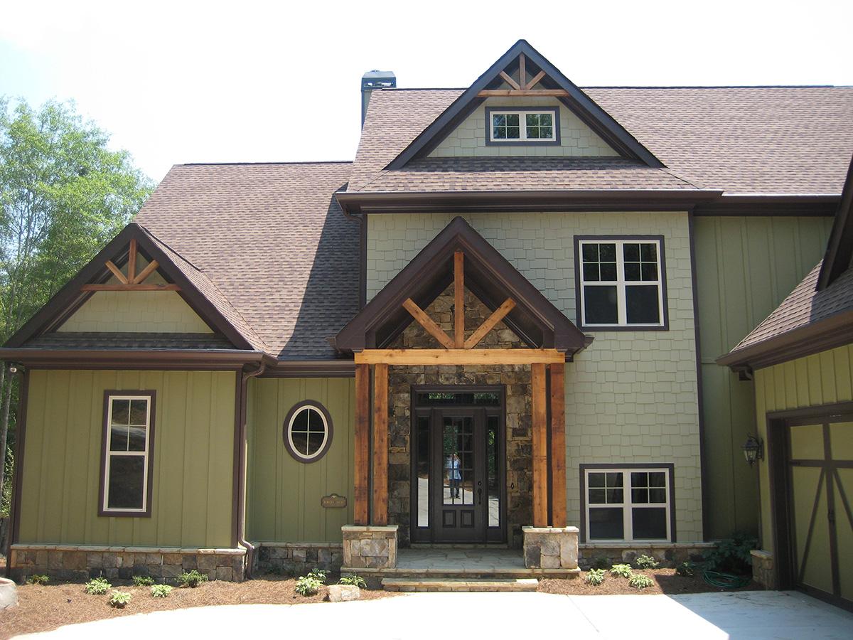 House plan exterior: Two-story home with prominent timber-framed entrance, gables, dormers, and stone accents.