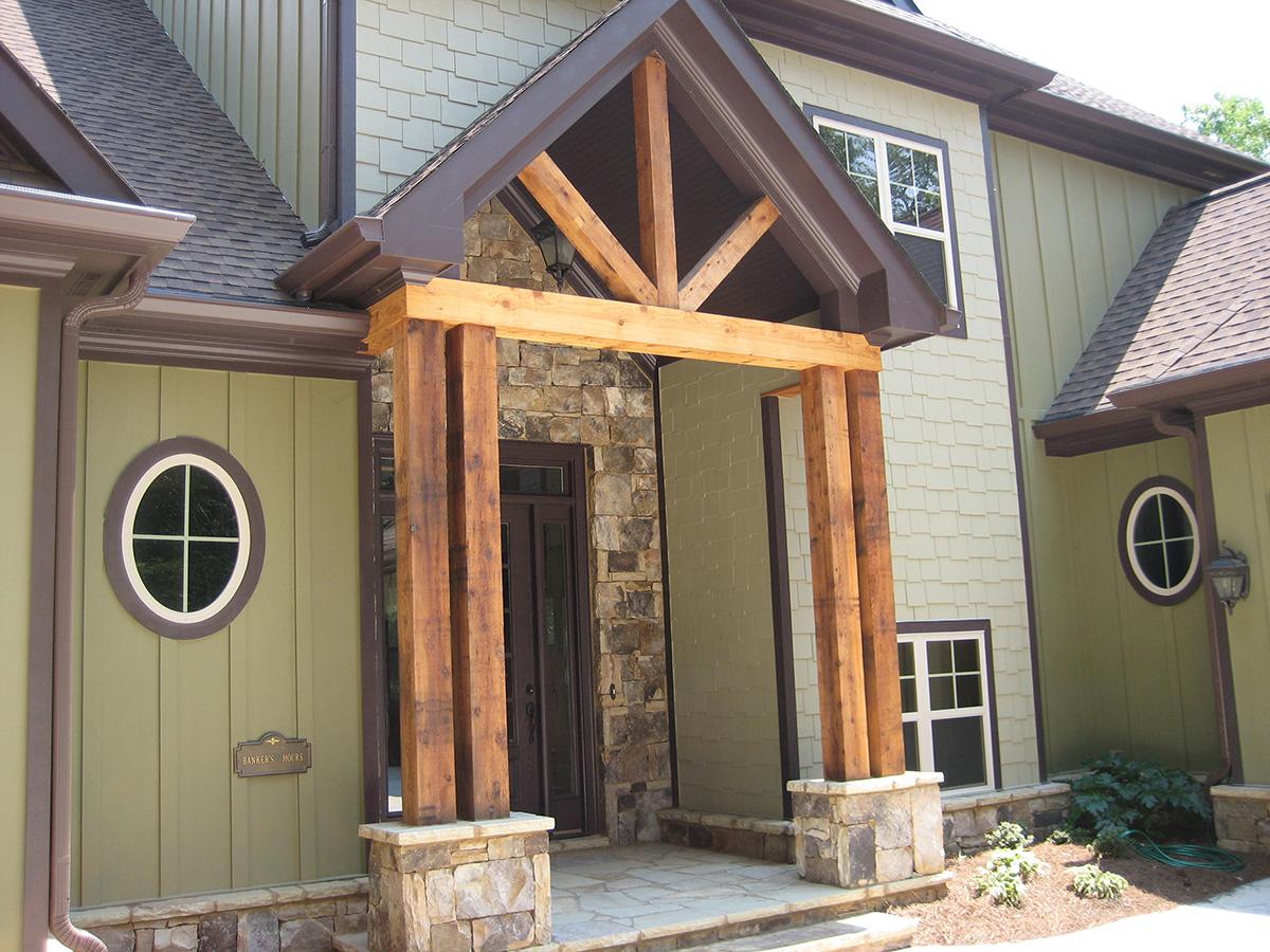 House plan exterior with stone foundation, wooden posts supporting a covered entryway, and circular windows.