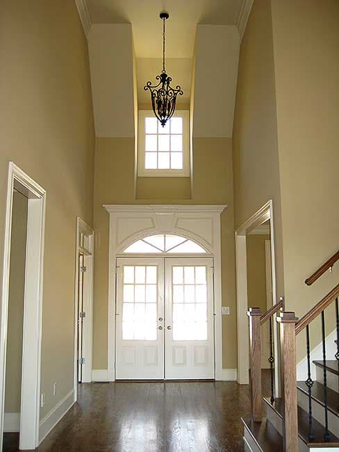 Foyer with double doors, transom window, vaulted ceiling, chandelier, and staircase.