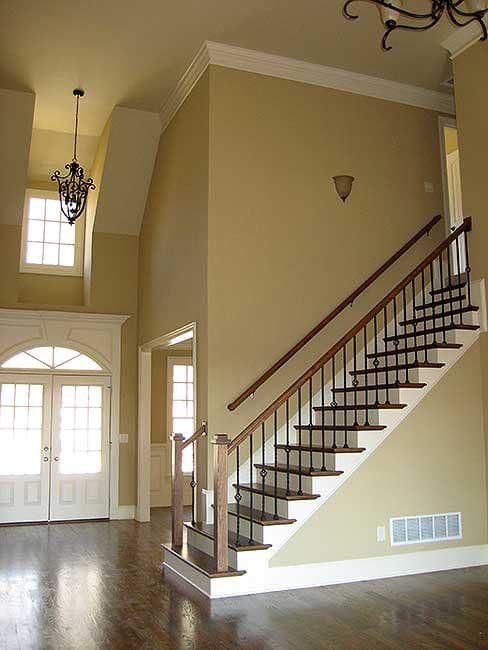 Interior view of a home foyer with a grand staircase, double doors with arched transom, and a vaulted ceiling.