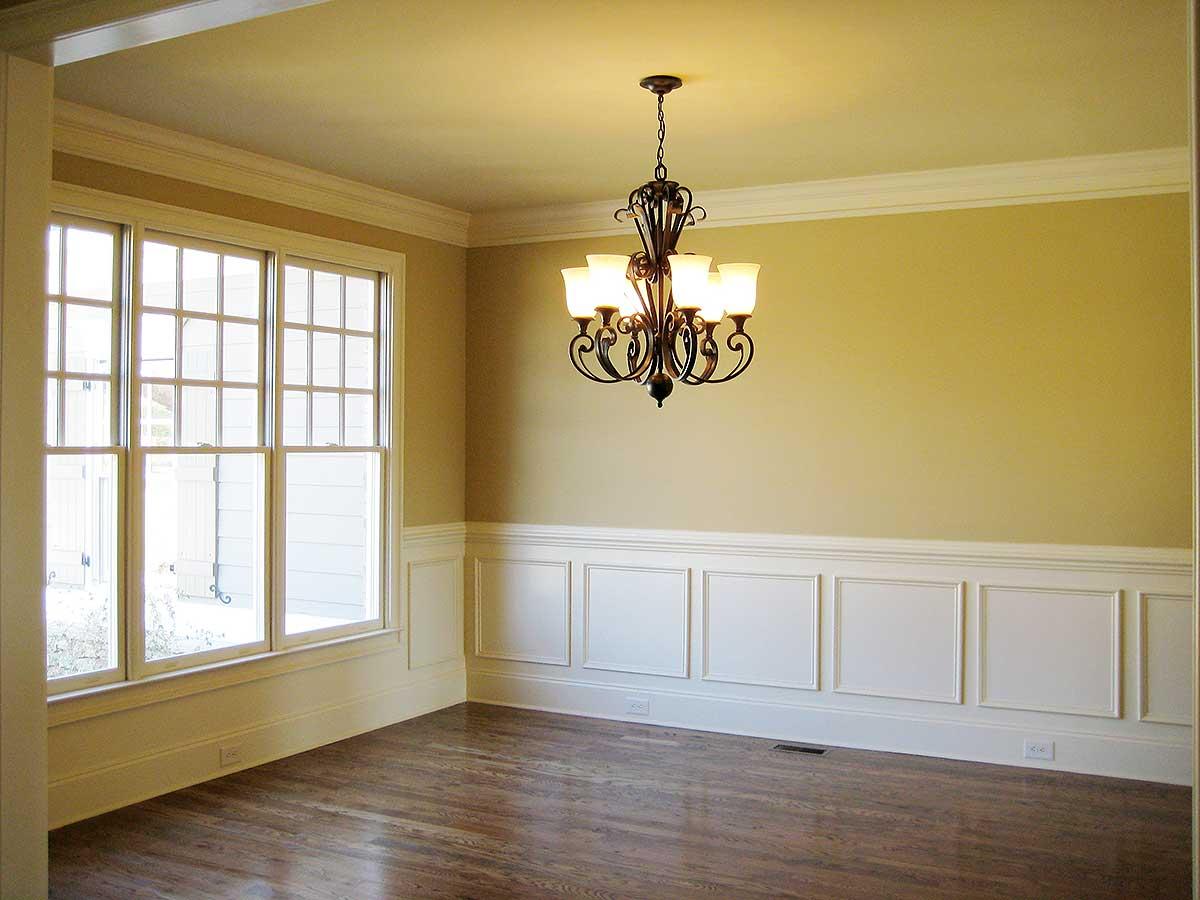 Interior view of a room with large grid windows, wainscoting, hardwood floors, and a chandelier.