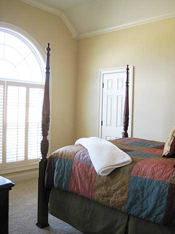 Bedroom with vaulted ceiling, four-poster bed, and arched window with white shutters.
