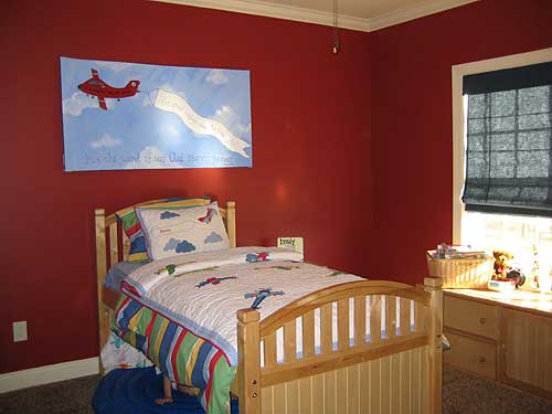 Children's bedroom with wood bed, airplane-themed bedding, and artwork of a red airplane with banner.