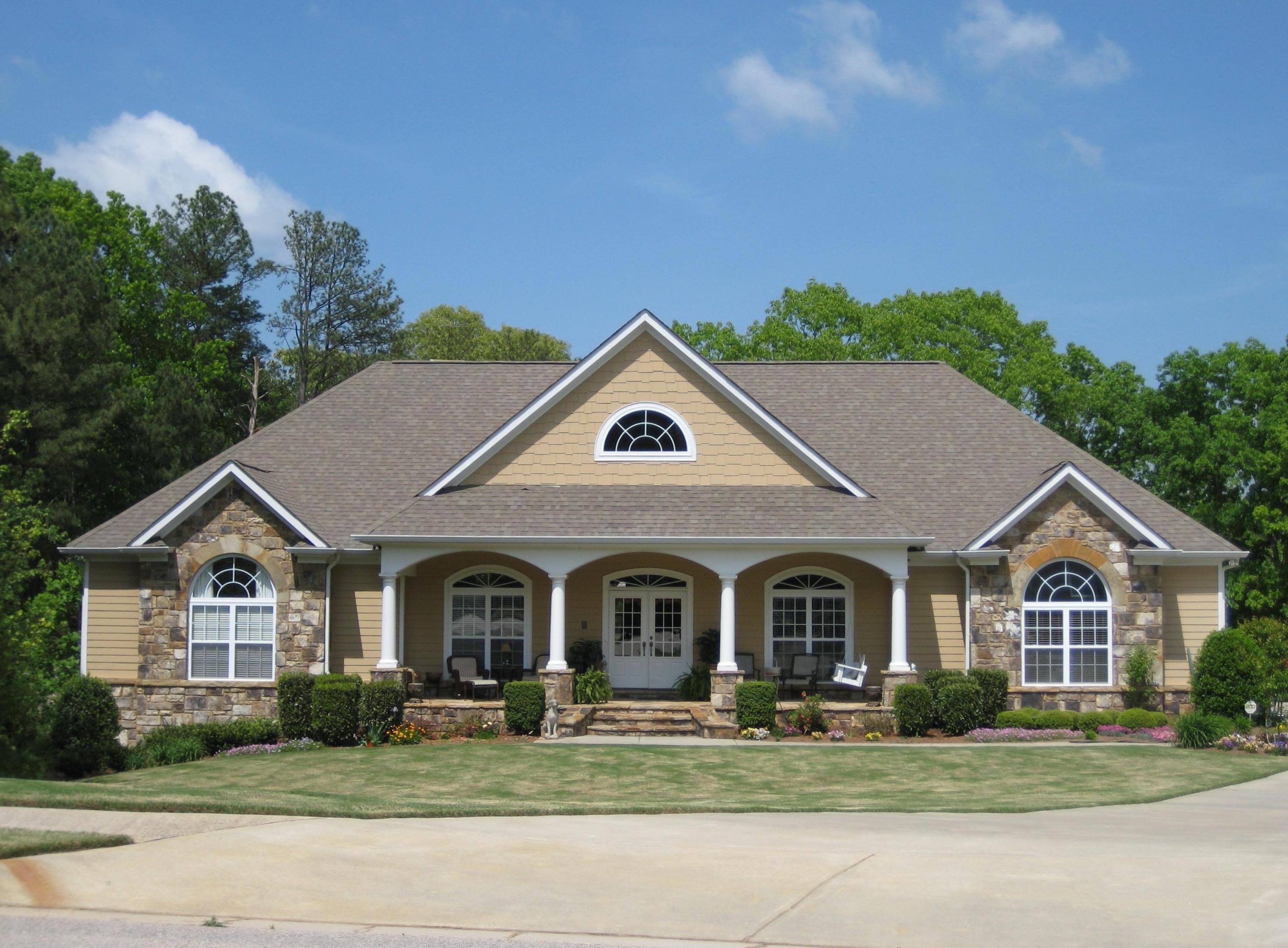 House plan exterior. Two-story, classic style with arched windows, a covered porch, gables, and stone accents.