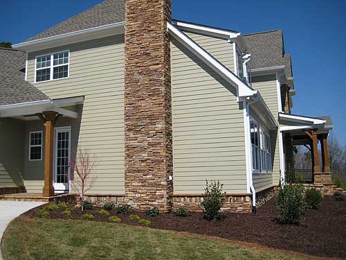 House plan exterior with stacked stone chimney, covered porch with wooden columns, and light green siding.