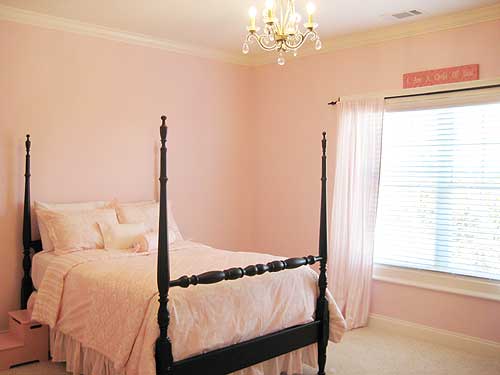 Bedroom interior with a four-poster bed, pink bedding, crystal chandelier, and window with curtains.