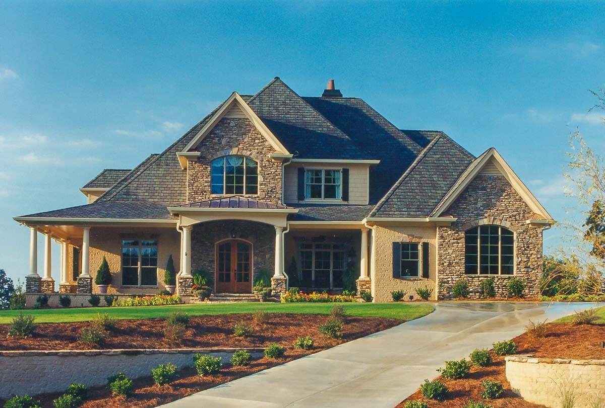 House plan exterior: Two-story home with stone accents, prominent gables, arched windows, and a covered front entry with columns.