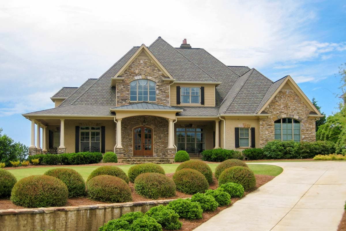 House plan exterior with stone accents, covered porch, and gabled roof. Features a two-story design with arched windows and a prominent entry.