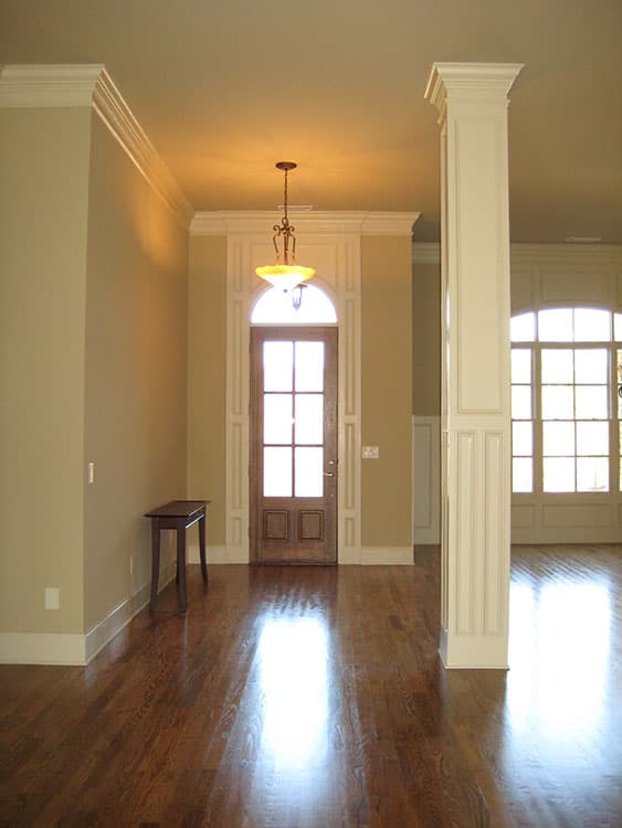 Interior view of a house entry with a wooden door, arched transom, decorative column, and large windows.