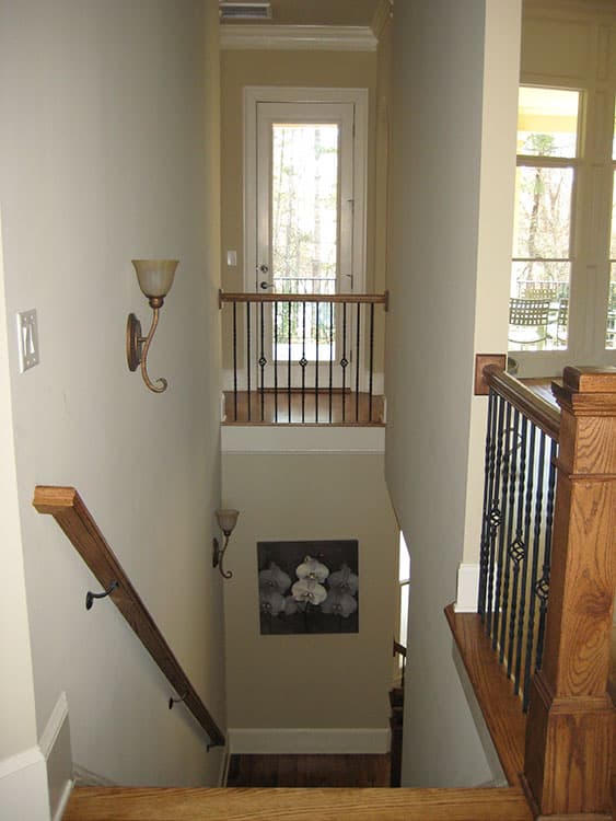 Interior view of a staircase with wooden banister, wrought iron spindles, and a door to a balcony.
