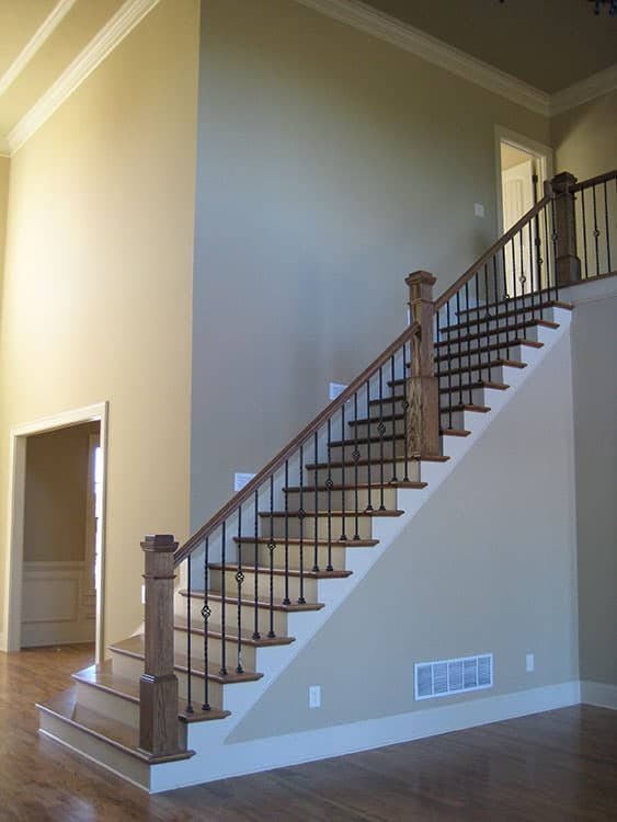 Interior view of a two-story foyer with a wooden staircase featuring ornate metal balusters and a dark wood handrail.
