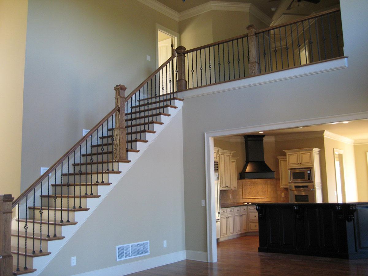 Two-story foyer with a turned staircase featuring ornate metal balusters and a wood handrail, open to a kitchen with cream cabinetry.