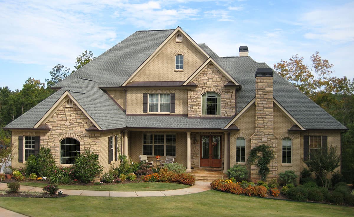 Two-story house plan exterior with stone accents, prominent gables, arched windows, and a covered front porch with double doors.