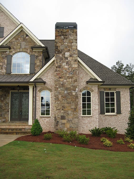 House plan exterior featuring stone chimney, arched windows, double doors, and gabled roof.