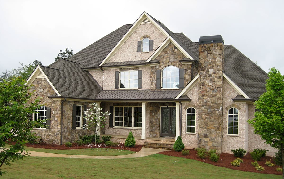 House plan exterior: Two-story home with stone and brick facade, prominent gables, arched windows, and covered front porch.