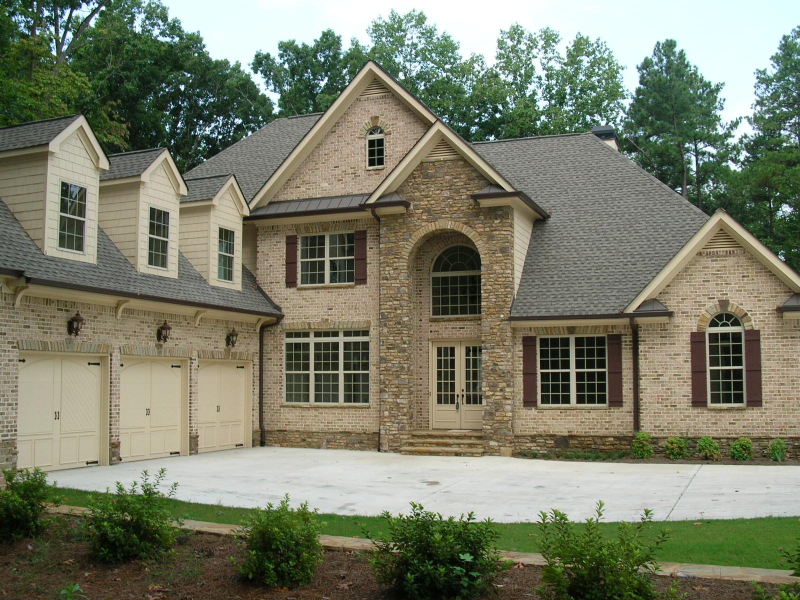 House plan exterior. Two-story brick home with stone accents. Features include arched entry, dormers, and attached three-car garage.
