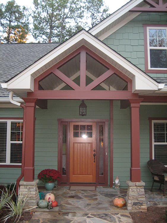 House plan exterior: Covered front porch with stone columns, wood door, glass sidelights, and decorative gable bracing.