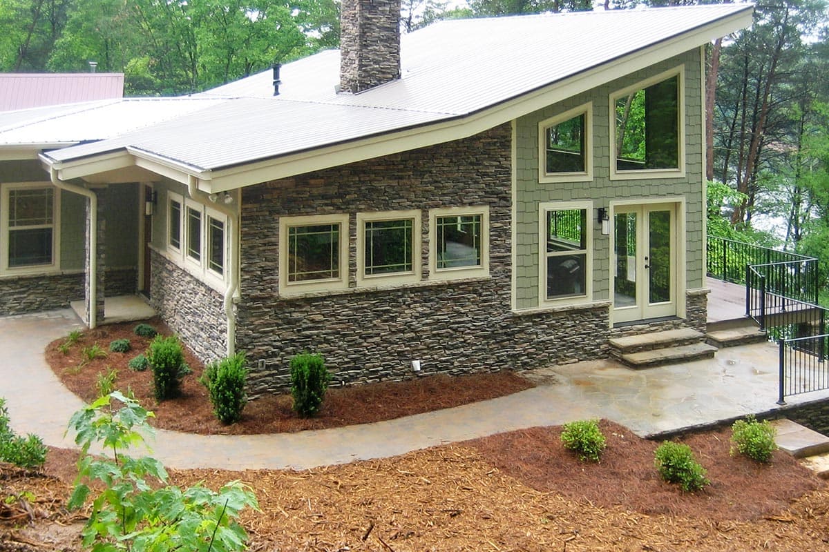 House plan exterior with a sloped roofline, stone veneer, and large, multi-paned windows.