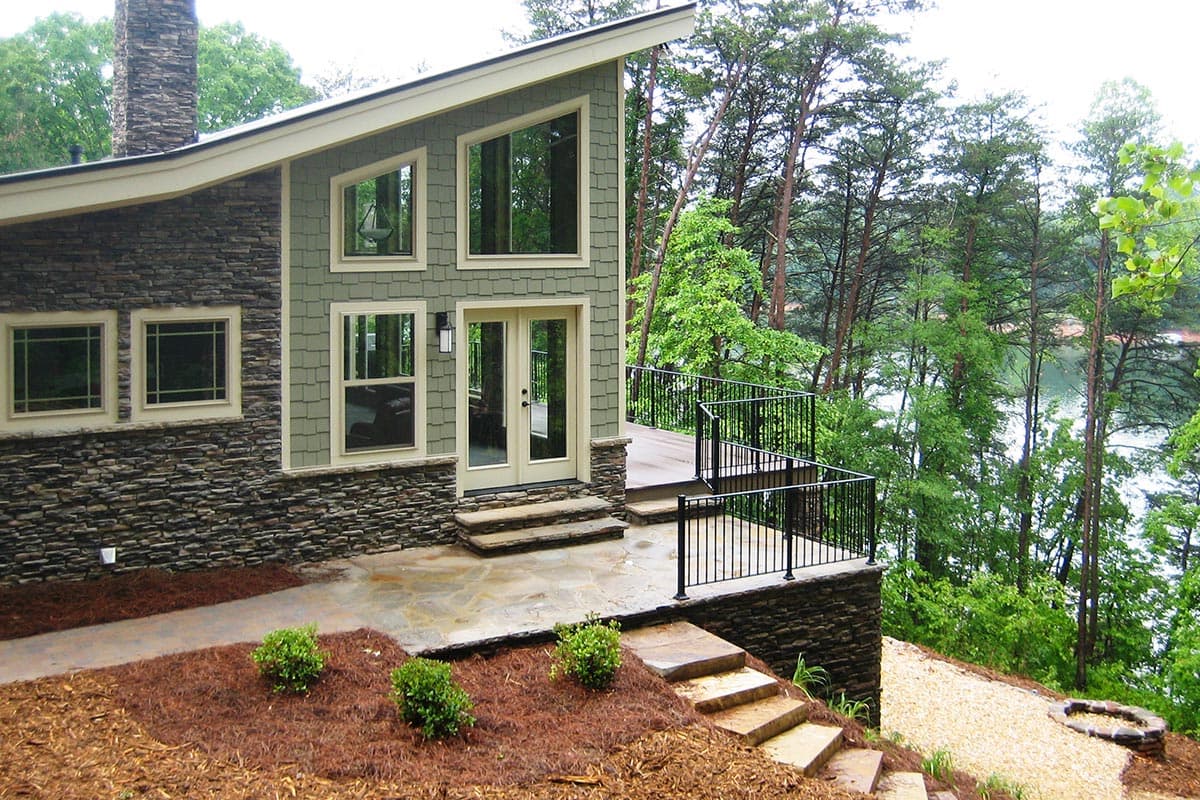 Modern house plan exterior with stacked stone base, asymmetric gables, multiple window styles, and a wraparound deck.
