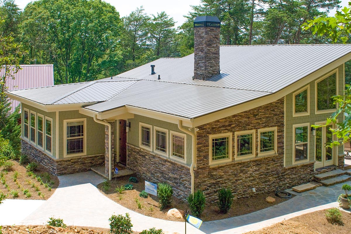 House plan exterior. One-story home with a stone and siding facade. Features include a metal roof, stacked stone chimney, and large windows.