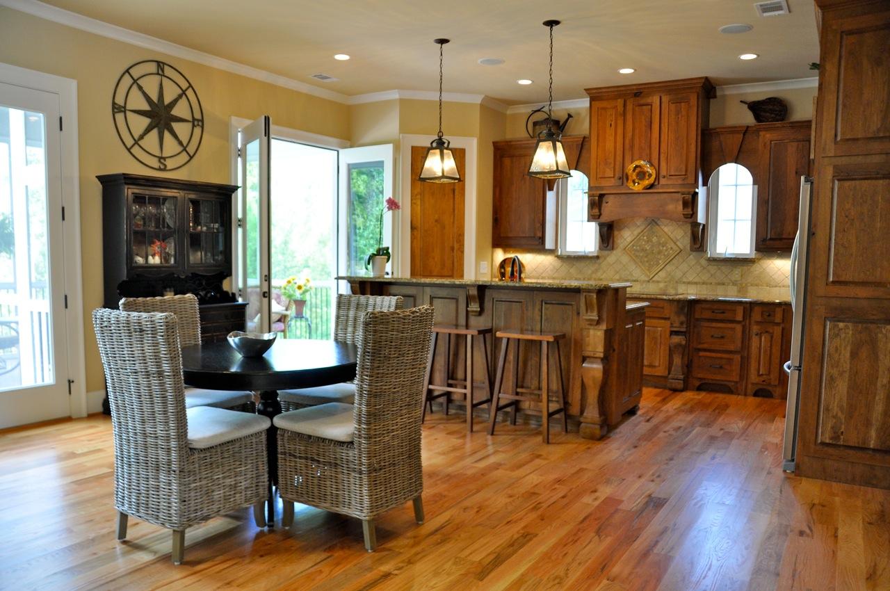 Kitchen with wood cabinetry, island with bar seating, dining table with wicker chairs, and double doors leading outside.