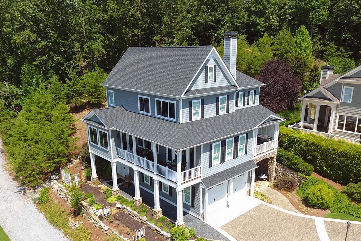 Three-story house plan exterior with a wrap-around porch, two-car garage, dormers, and layered rooflines.
