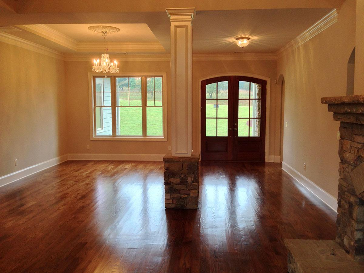 Interior view of a room with hardwood floors, a stone-clad pillar, a crystal chandelier, and double arched doors.