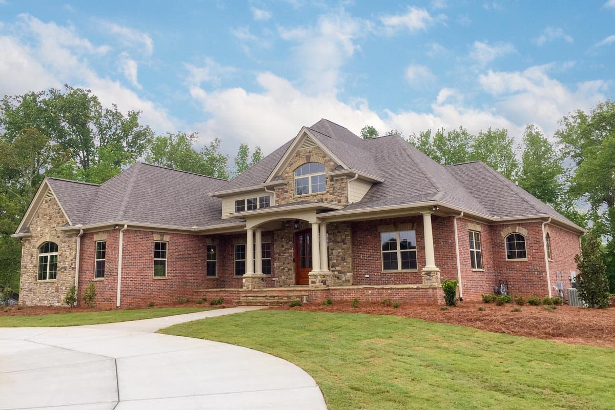 House plan exterior: brick, stone accents, prominent gabled entrance with columns, arched windows, and multiple rooflines.
